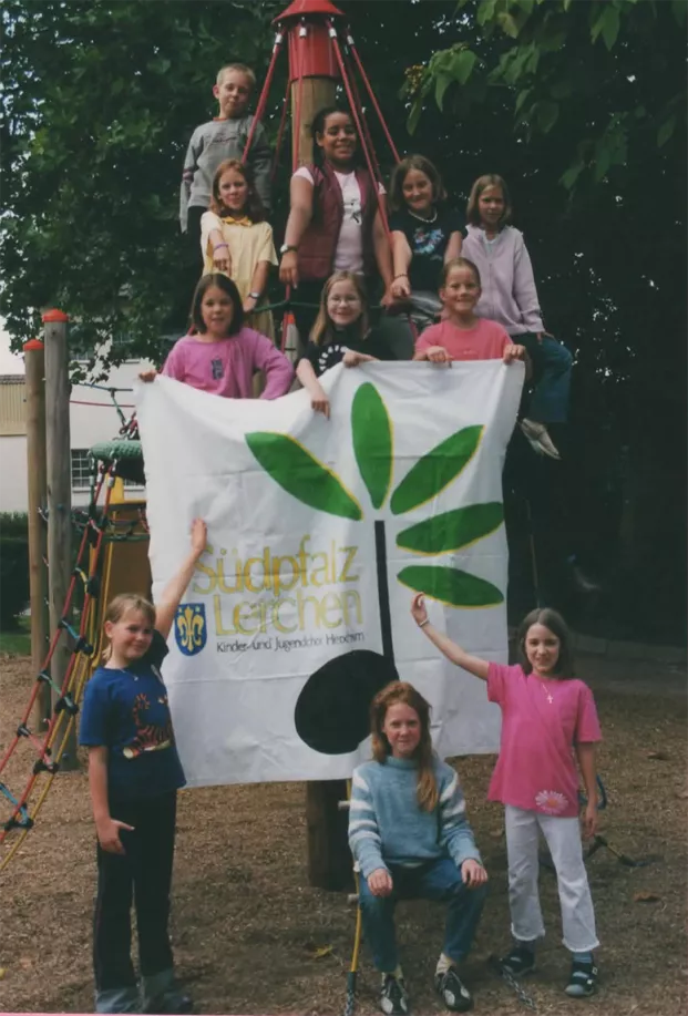 Kinder der Südpfalz Lerchen auf einem Klettergerüst halten das Chor-Logoplakat hoch