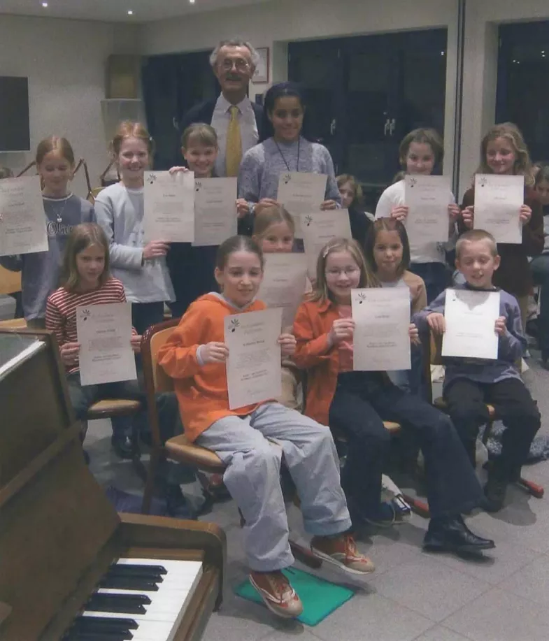 Kinder halten stolz ihre Urkunden hoch neben einem Chorleiter und einem Klavier