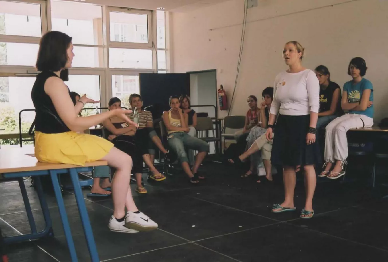 Gesangsworkshop in einem hellen Raum mit zwei stehenden Sängerinnen und sitzenden Jugendlichen