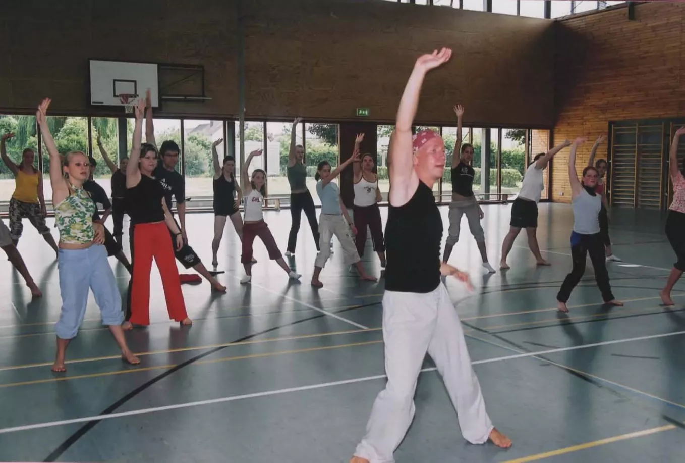 Tanzworkshop in einer Sporthalle mit vielen Teilnehmerinnen und einem Trainer mit erhobenen Armen
