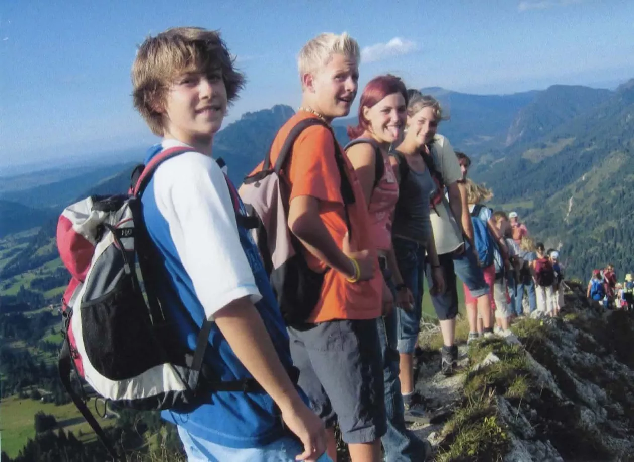Jugendliche mit Rucksäcken bei einer Bergwanderung auf einem sonnigen Grat mit Alpenpanorama