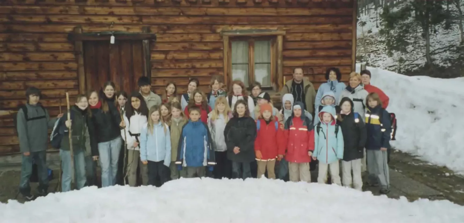 Winterliches Gruppenfoto der Chorferien vor einer Blockhütte mit Schneewall