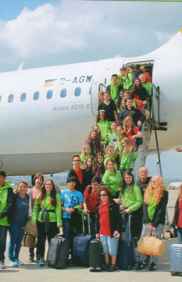 Chorgruppe in grünen Jacken mit Koffern vor einem Airbus A319 beim Abflug zur Chorreise