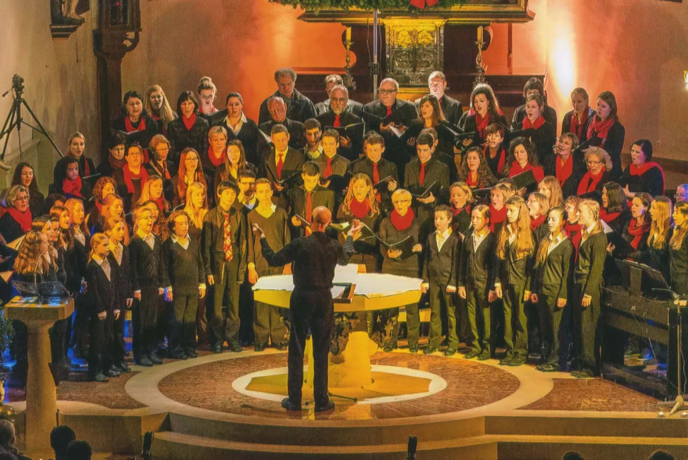 Projektchor mit roten Schals bei einem Weihnachtskonzert in einer festlich geschmückten Kirche