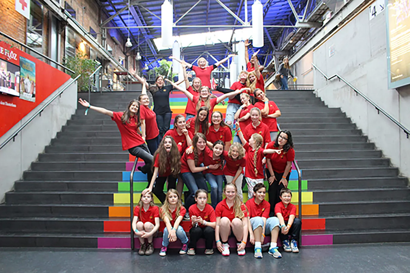 Chor in roten Poloshirts posiert ausgelassen auf einer bunten Regenbogentreppe beim Chorfest in Stuttgart