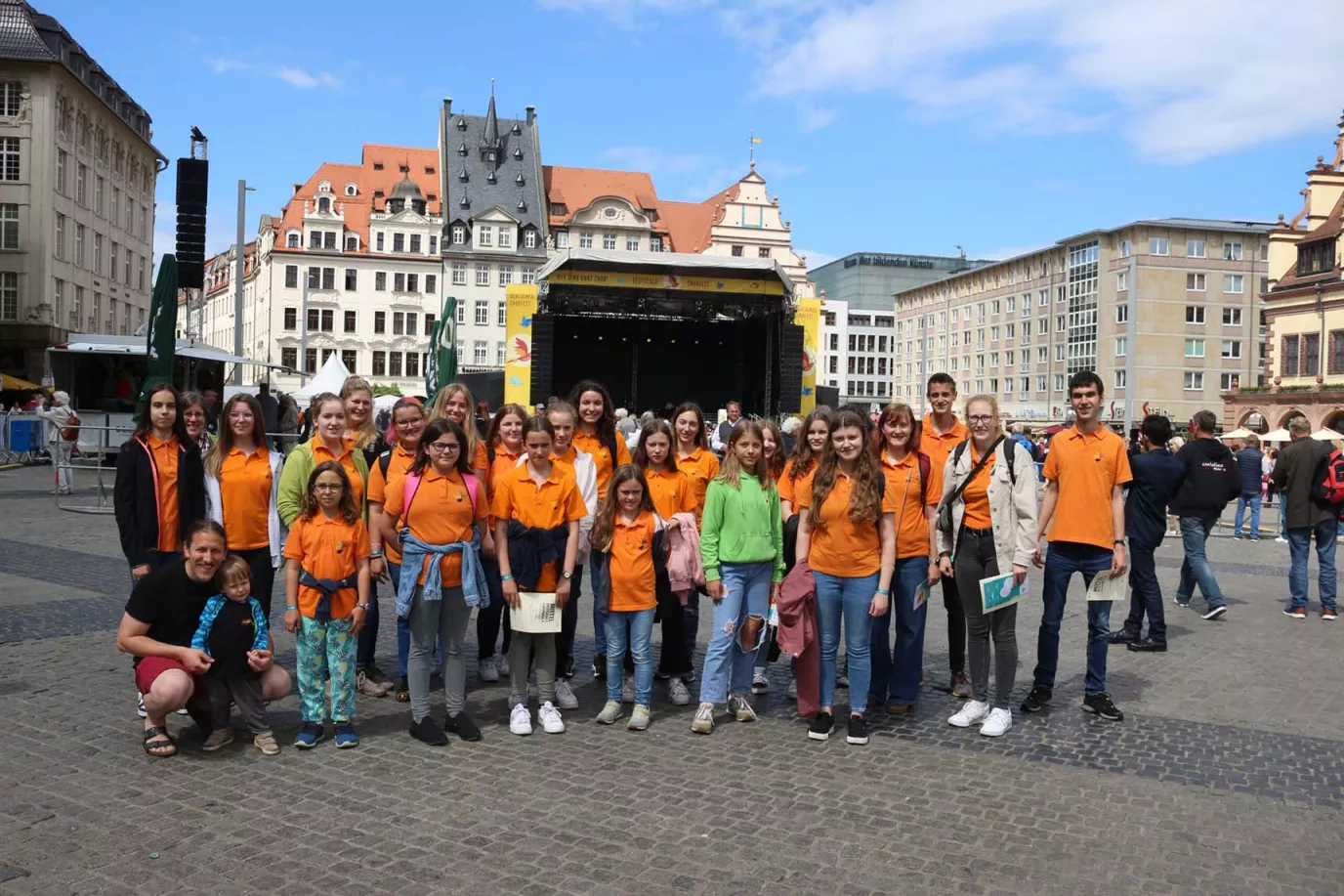 Chor in orangefarbenen Poloshirts auf dem Leipziger Marktplatz vor der Bühne des Deutschen Chorfests