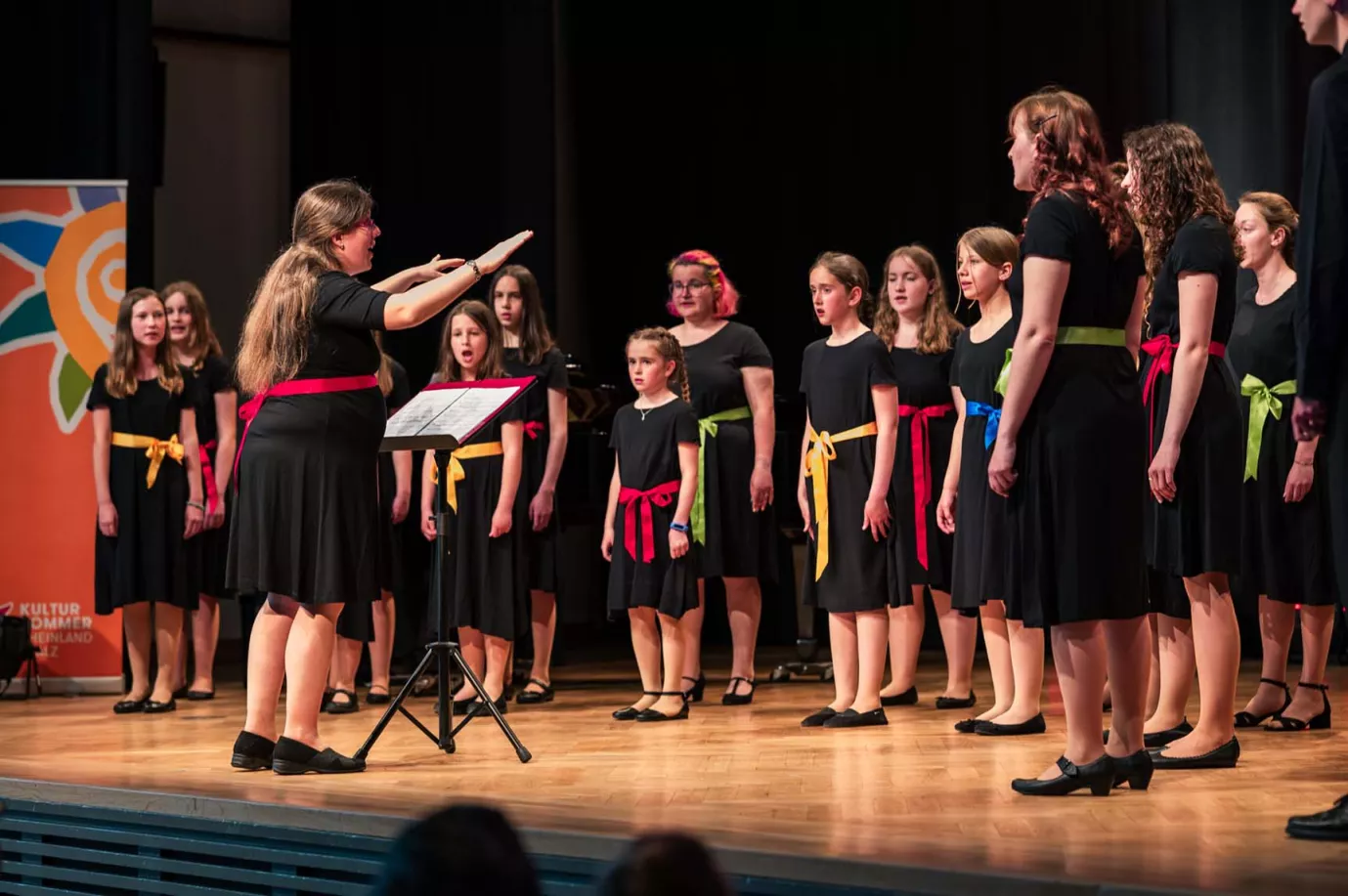 Chor in schwarzer Kleidung mit bunten Schärpen singt mit Dirigentin bei der Eröffnung des Kultursommers