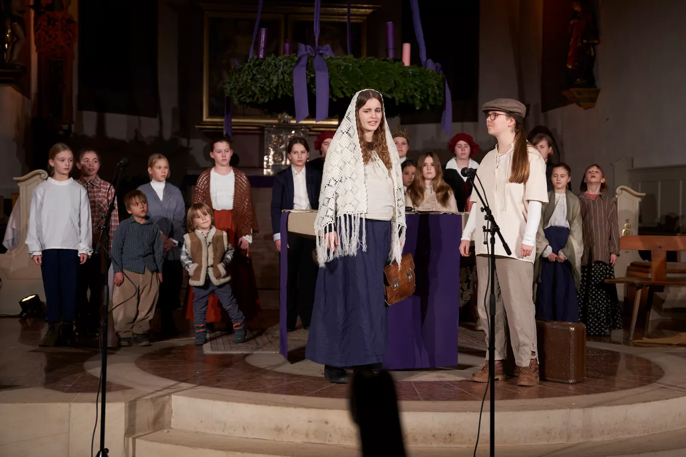 Kinder und Jugendliche in historischen Kostümen singen unter dem Adventskranz in der Kirche