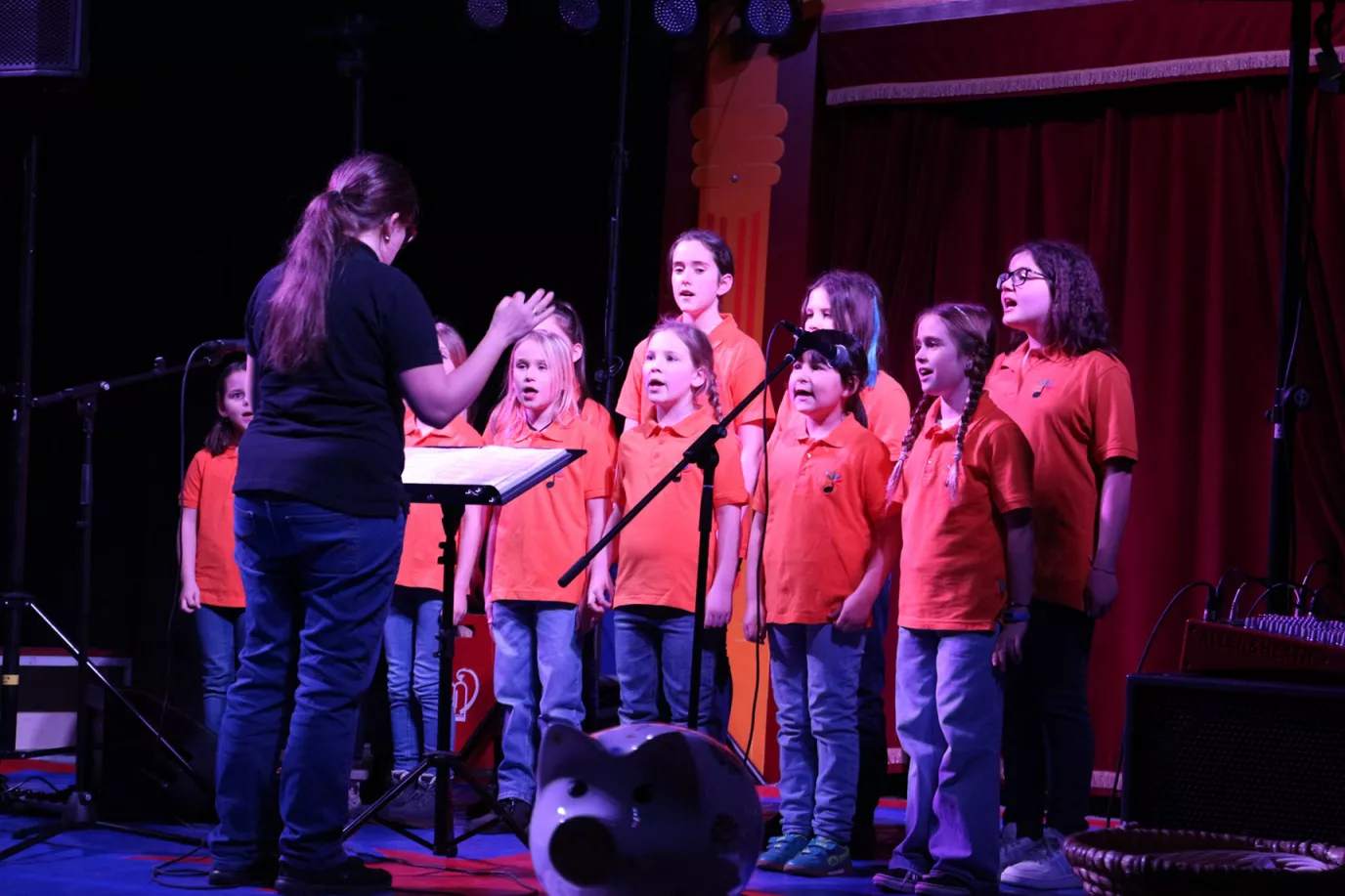 Kinderchor in roten Poloshirts singt mit Dirigentin auf einer Bühne im Zirkuszelt der Grundschule