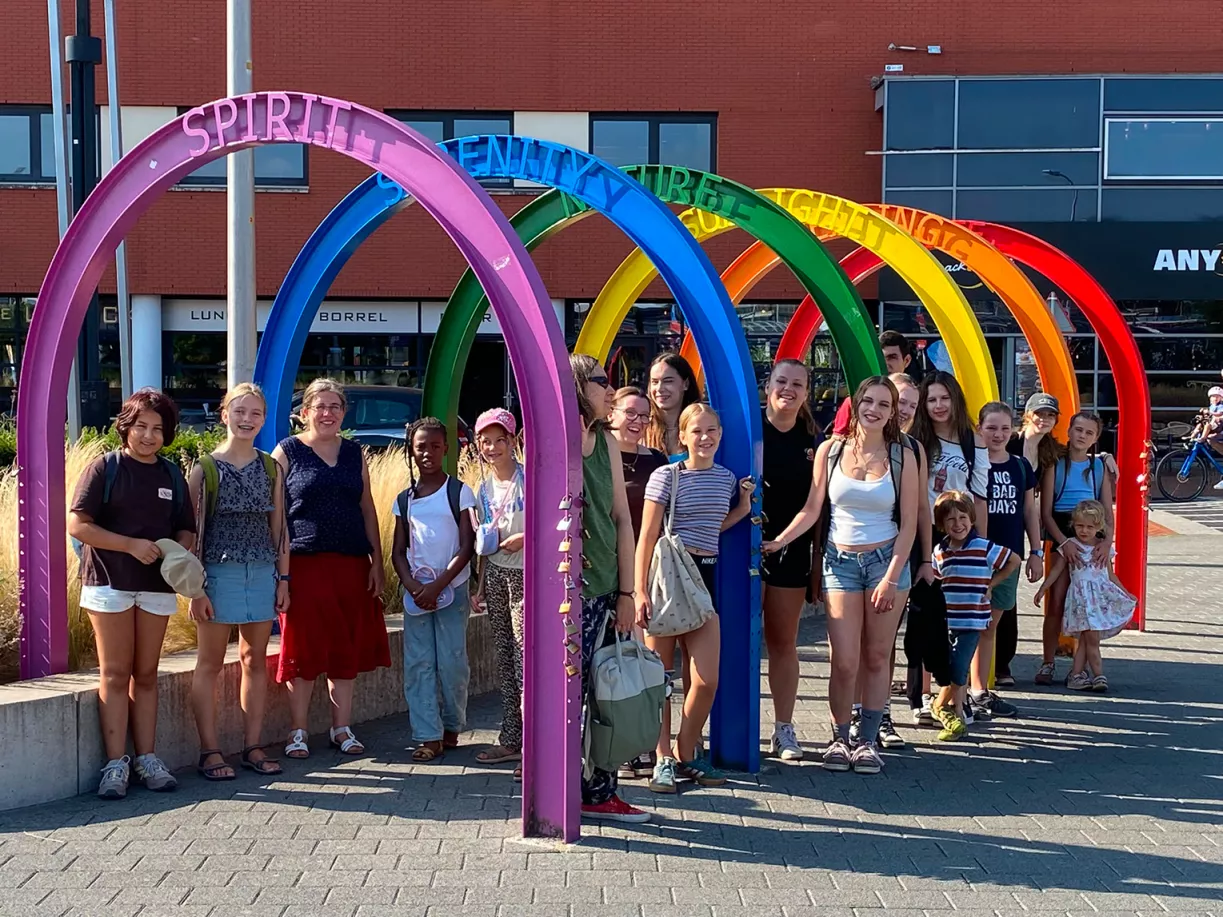 Chorgruppe posiert vor einem bunten Regenbogenbogen mit den Schriftzügen Spirit, Serenity und Nature bei den Chorferien