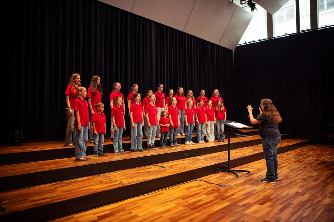 Kinderchor in roten Poloshirts singt mit Dirigentin auf einer Bühne beim Chorfest in Nürnberg