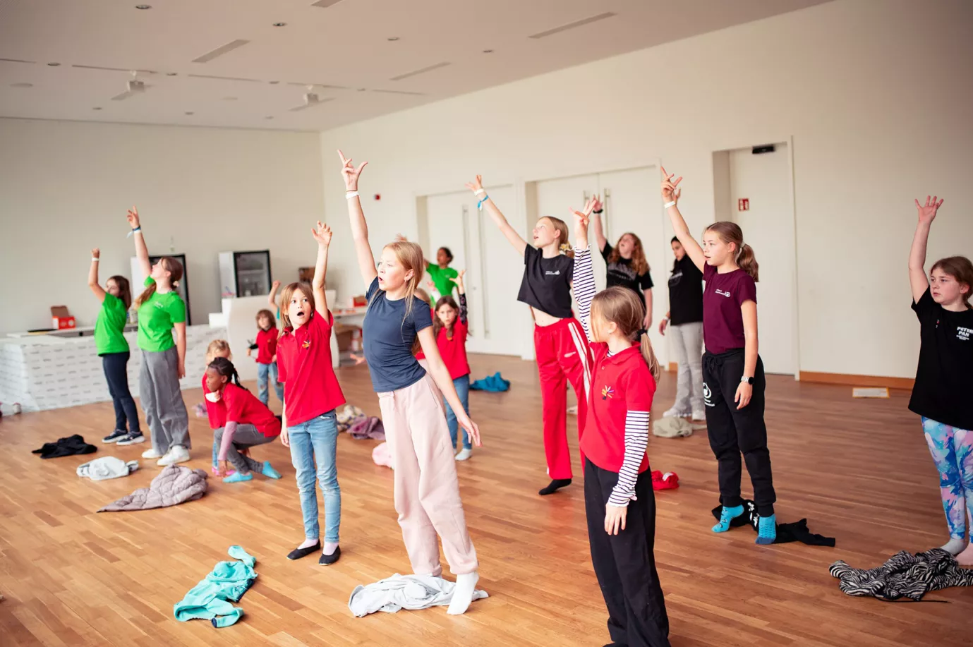 Kinder und Jugendliche üben mit erhobenen Armen eine Choreografie in einem hellen Probenraum beim EJMF