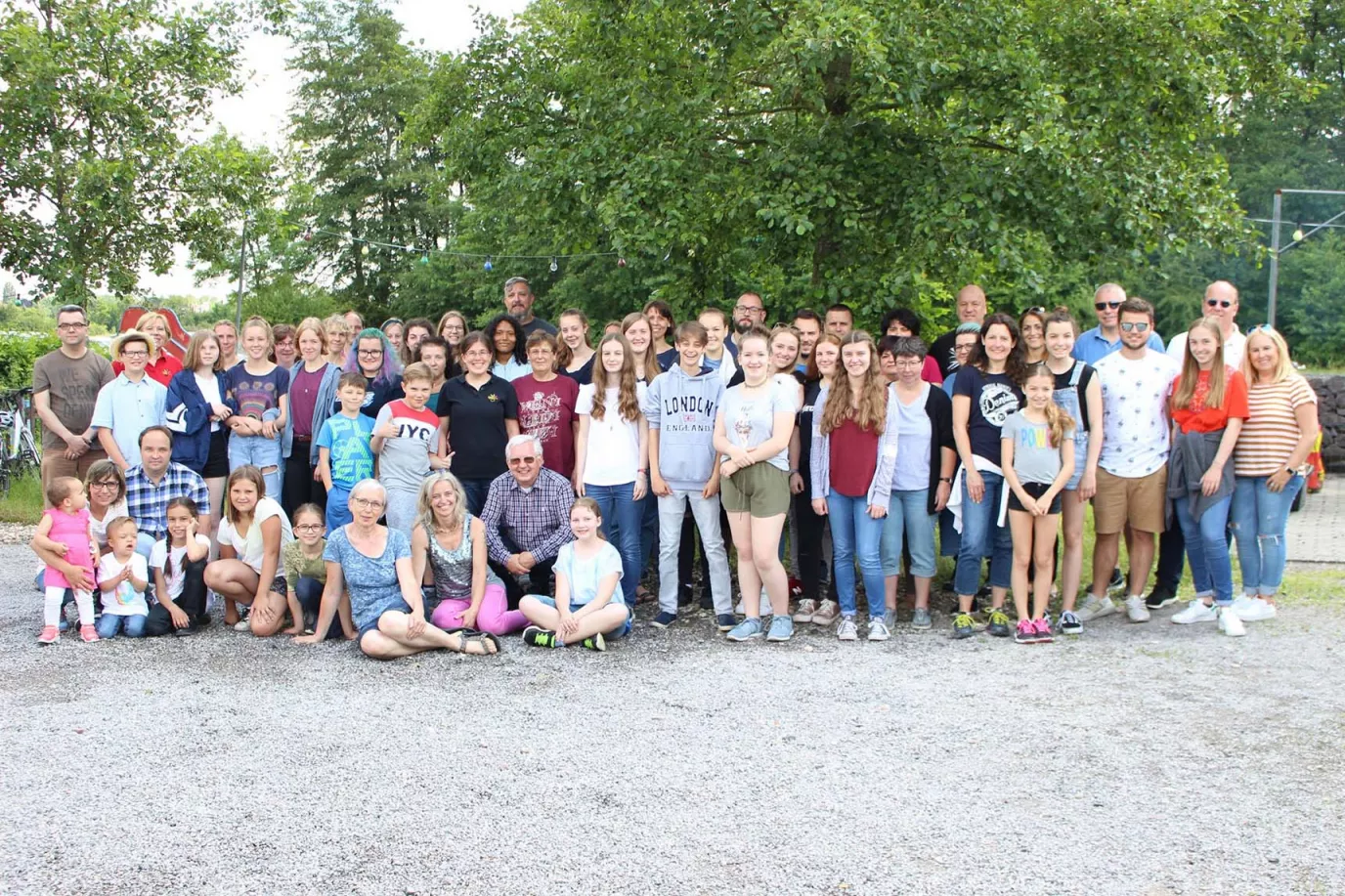 Großes Gruppenfoto von Chormitgliedern und Familien beim Familientag unter einem Baum