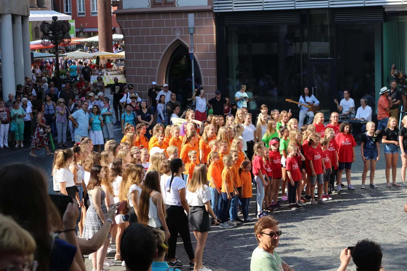Mehrere Chöre in bunten Shirts singen beim Landeschorfest in der Mainzer Innenstadt vor Publikum