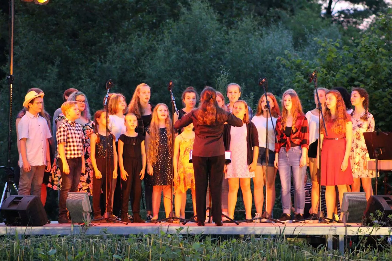 Chor singt in der Abenddämmerung bei einem Open-Air-Konzert am See mit Dirigentin